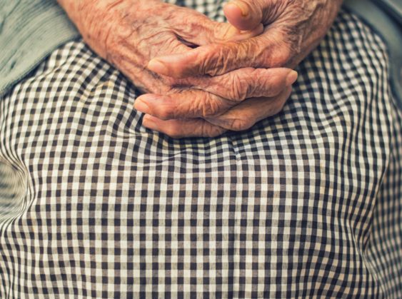 Elderly hands folded across a woman's lap